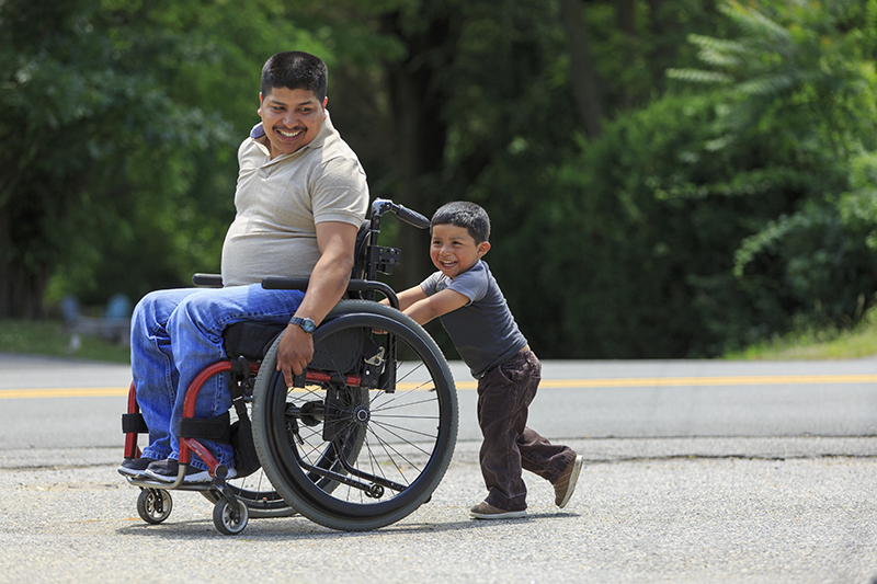 Child pushing man in a wheelchair.